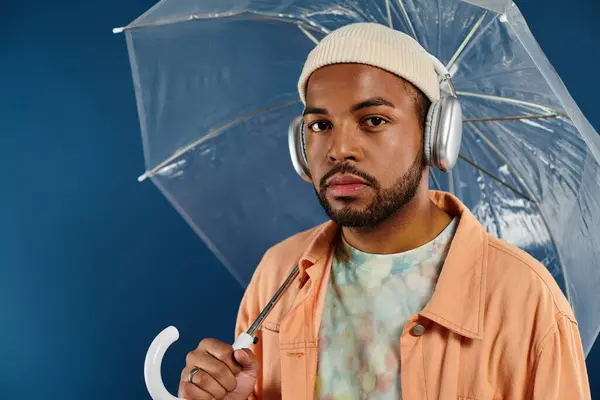 Stylish man with headphones holding umbrella against vibrant backdrop. — Stock Photo