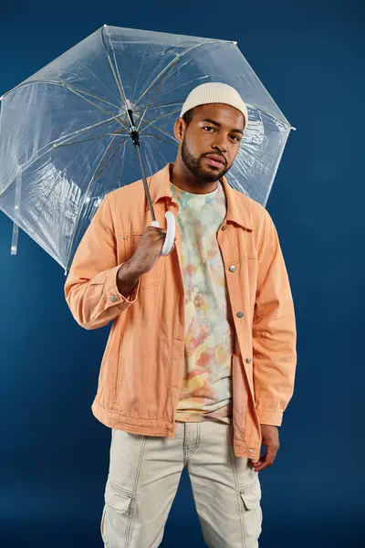 A stylish African American man holding a clear umbrella over his head against a vibrant backdrop. — Stock Photo