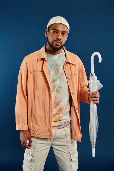 Elegante uomo afroamericano posa con ombrello sullo sfondo vibrante. — Foto stock