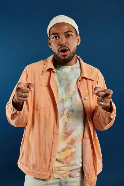 Stylish African American man striking a pose in a vibrant backdrop wearing an orange jacket and white hat. — Stock Photo