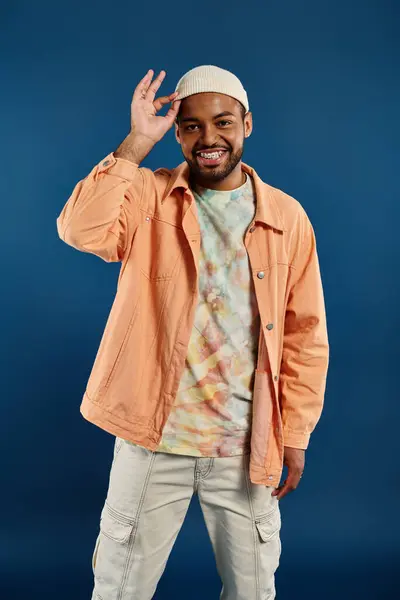 Homme afro-américain élégant posant sur fond vibrant veste orange et chapeau blanc. — Photo de stock