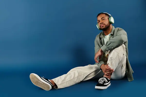 Stylish African American man sitting on floor, lost in music with headphones on. — Stock Photo