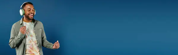 Stylish African American man with headphones standing in front of vibrant blue backdrop. — Stock Photo