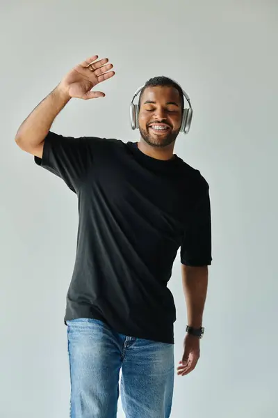 A stylish African American man, wearing headphones and a black shirt, poses against a vibrant backdrop. — Stock Photo