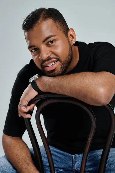 Stylish African American man sitting on top of a wooden chair against a vibrant backdrop. — Stock Photo