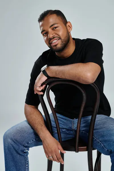 Stylish African American man sitting gracefully on a wooden chair against a vibrant backdrop. — Stock Photo