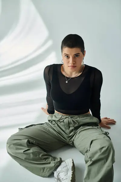 Una giovane donna con i capelli corti seduta a terra vestita in elegante abbigliamento casual. — Foto stock