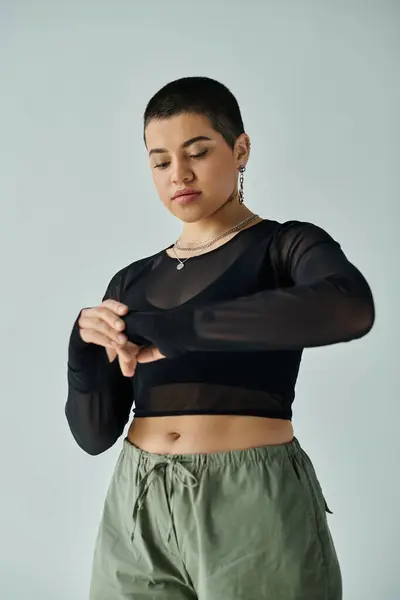 Uma jovem mulher com cabelo curto marcando uma pose em traje casual elegante contra um fundo cinza. — Fotografia de Stock