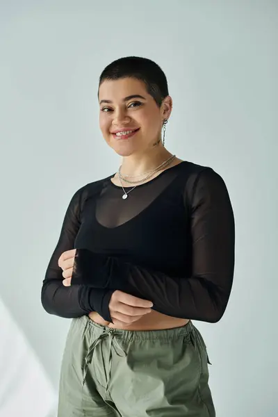 A young woman with short hair strikes a pose in trendy casual clothing against a grey background. — Stock Photo