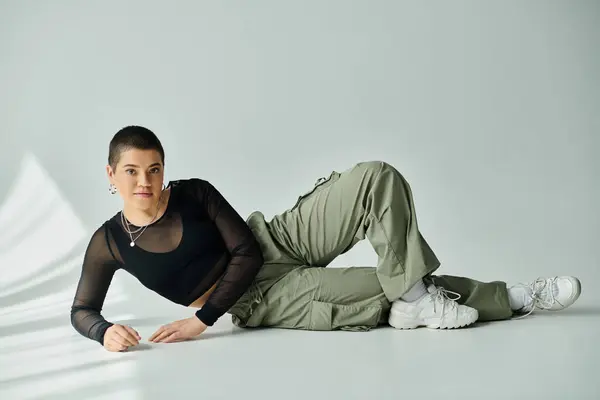 A young woman with short hair lies on the ground in a black shirt and khaki pants, exuding peacefulness. — Stock Photo