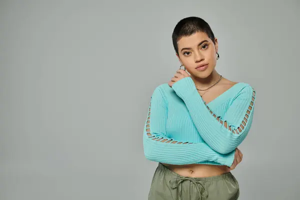 A young woman with short hair strikes a pose in a stylish blue sweater against a neutral grey backdrop. — Stock Photo