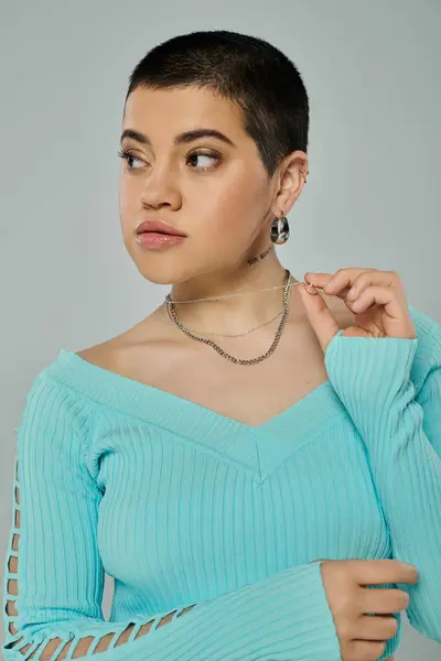 Young woman with short hair strikes a pose, wearing a blue sweater on a grey background. — Stock Photo