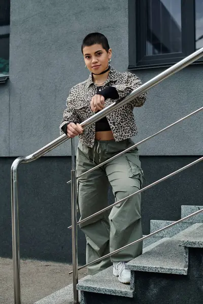 Stylish young woman with short hair balances on stair rail near modern building, showcasing daring grace. — Stock Photo