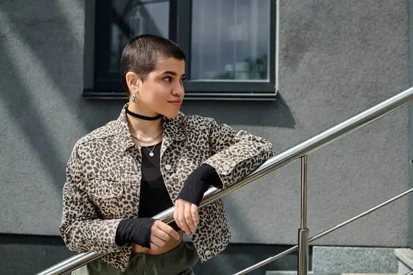 A young woman with short hair and a leopard print jacket standing on the steps of a modern building. — Stock Photo