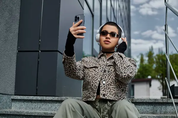 Young woman with modern style, holding cellphone, sitting on steps outside building. — Stock Photo