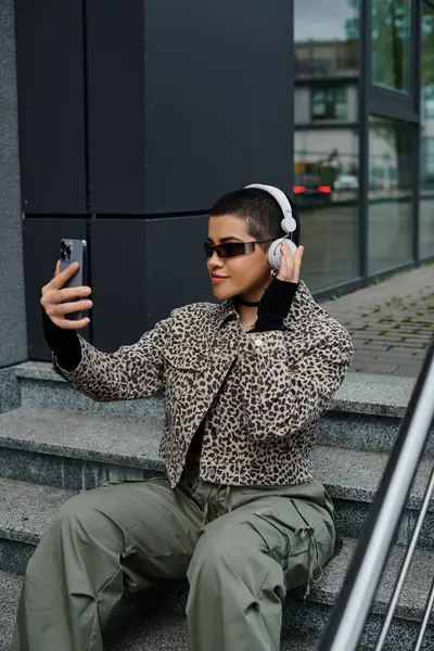 A stylish woman in urban setting sits on stairs, holding cell phone. — Stock Photo
