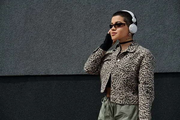 A stylish woman in leopard print jacket walks down a city street while listening to music on headphones. — Stock Photo