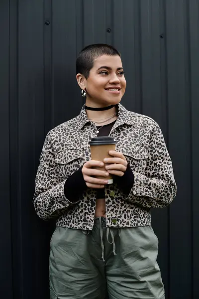 Young woman with short hair stands stylishly sipping coffee in front of a black wall. — Stock Photo