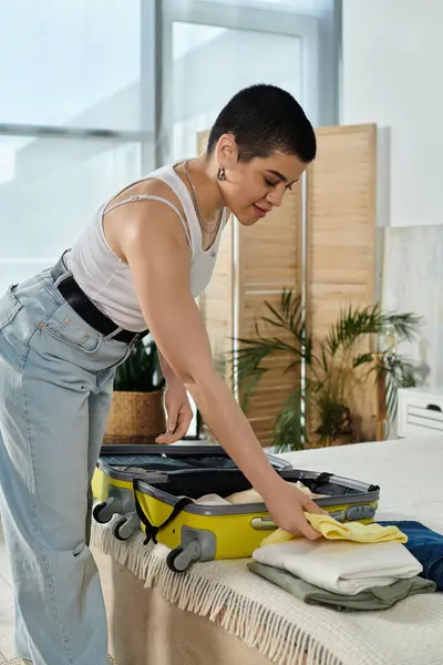 A young woman with short hair cleans a bed while packing a yellow suitcase for an upcoming vacation and trip. — Stock Photo