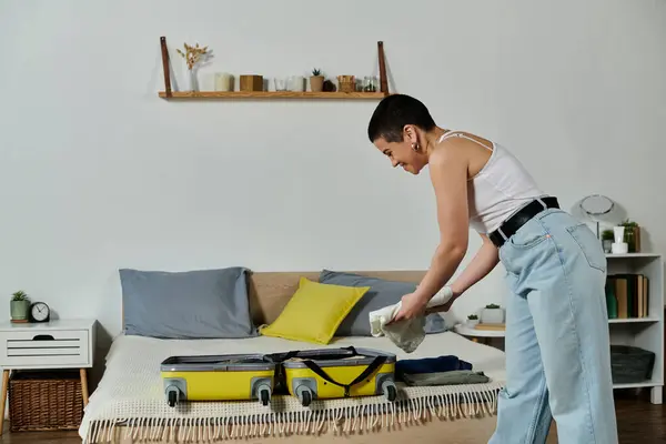 Young woman with short hair tidying bed and packing yellow suitcase for a vacation and trip at home. — Stock Photo