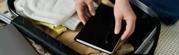 Mujer joven recortada cuidadosamente coloca un libro dentro de una maleta, preparándose para unas vacaciones aventureras. - foto de stock
