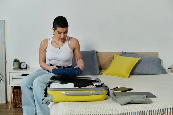 A young woman with short hair sits on a bed, packing her luggage, preparing for an upcoming vacation or trip. — Stock Photo
