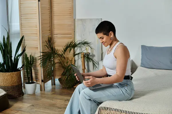 Young woman with short hair lounging on bed, fixated on laptop in casual wear at home. — Stock Photo