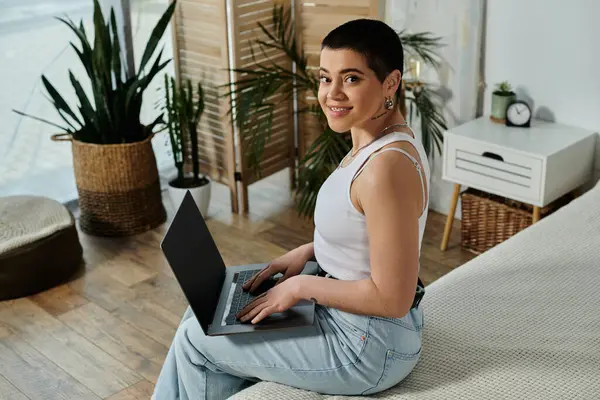 A young woman with short hair sits on a bed, engrossed in her laptop. — Stock Photo