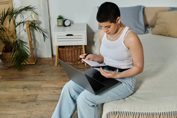 Young woman with short hair sitting on bed, engaged with laptop computer, embodying modern technology and connectivity. — Stock Photo