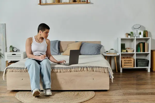 Una mujer joven con el pelo corto, en ropa casual, se sienta relajado en un sofá, absorto en el uso de un ordenador portátil. — Stock Photo