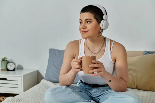 Casual young woman with short hair sitting on bed, enjoying a cup of coffee. — Stock Photo