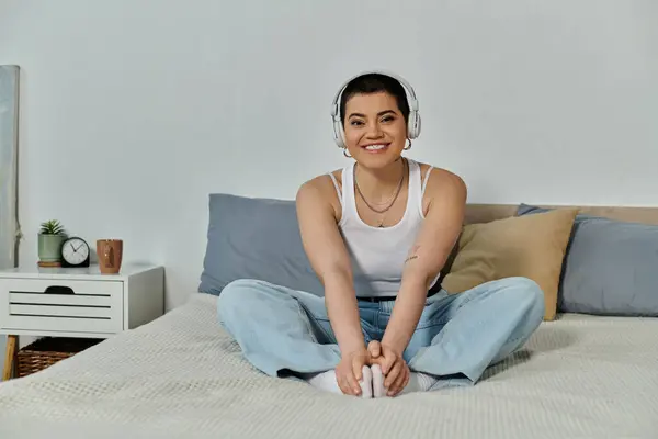 A woman with short hair enjoys music, sitting on a bed wearing headphones. — Stock Photo