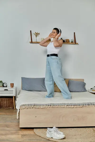 Young woman with short hair stands atop bed in cozy room, embodying peace and tranquility. — Stock Photo