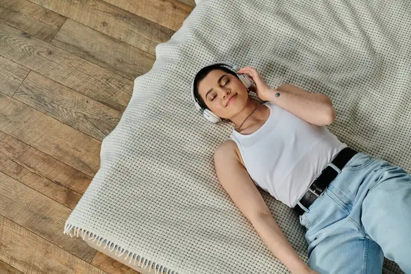 A young woman with short hair lounges on a bed in a cozy wooden home setting, exuding peace and tranquility. — Stock Photo