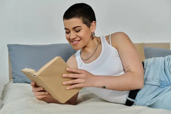 Eine junge Frau mit kurzen Haaren entspannt sich auf einem Bett, vertieft in ein Buch. — Stockfoto