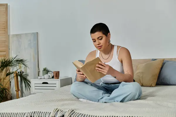 Una mujer con el pelo corto en traje casual, inmersa en la lectura mientras está sentada en una cama. — Stock Photo