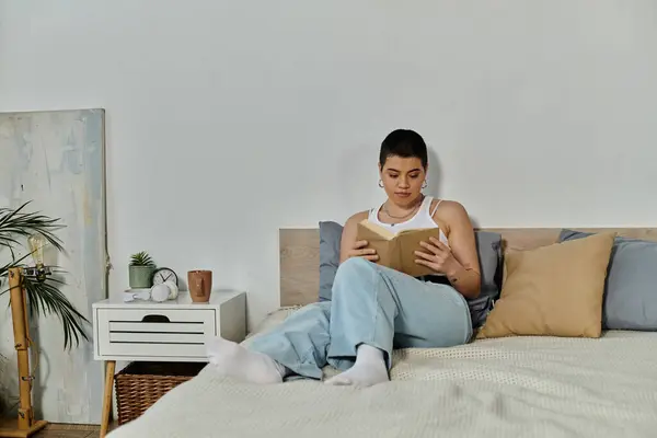 A woman with short hair relaxes on a bed, engrossed in a book, surrounded by a cozy atmosphere. — Stock Photo