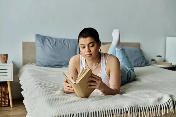 A young woman with short hair relaxes in casual wear, engrossed in a book while lying on a cozy bed. — Stock Photo