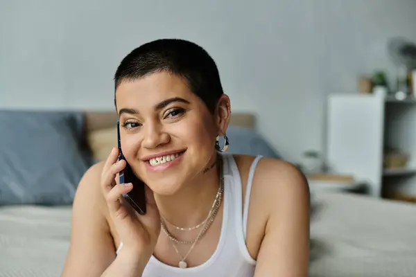 Young woman in casual wear, sitting on bed, talking on cell phone. — Stock Photo