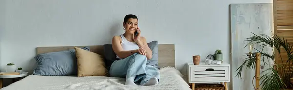 A woman in casual wear with short hair sitting on a bed, engaged in conversation on a cell phone. — Stock Photo