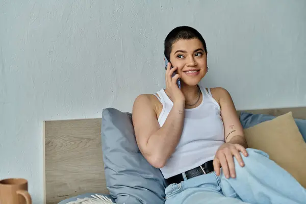 A casually dressed young woman with short hair sitting on a bed, engrossed in a phone conversation. — Stock Photo