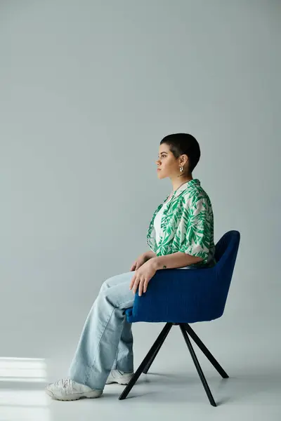 Eine junge Frau mit kurzen Haaren sitzt in gelassener Pose auf einem blauen Stuhl.. — Stock Photo