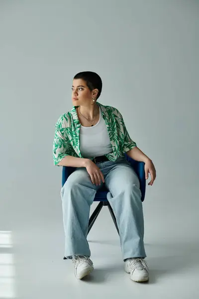 Une jeune femme aux cheveux courts s'assoit gracieusement sur une chaise bleue vibrante d'une manière détendue et calme. — Photo de stock