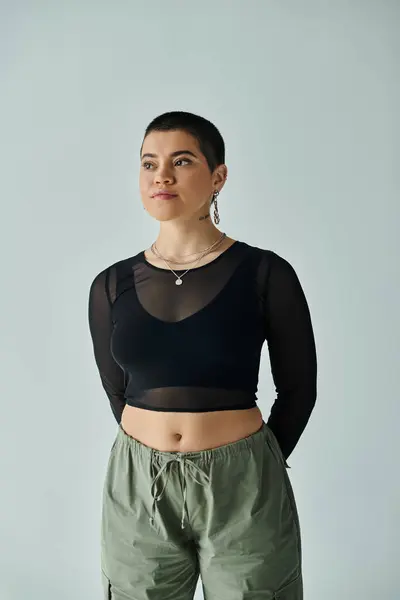 Una joven con el pelo corto posa en un elegante atuendo casual sobre un fondo gris. - foto de stock