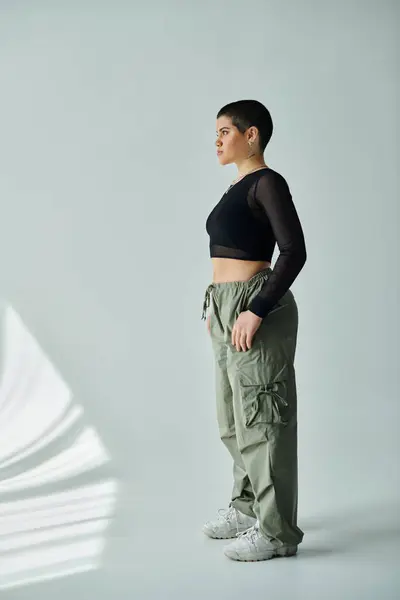 Una mujer joven y elegante con el pelo corto alcanza una pose en elegante atuendo casual contra un fondo blanco. - foto de stock