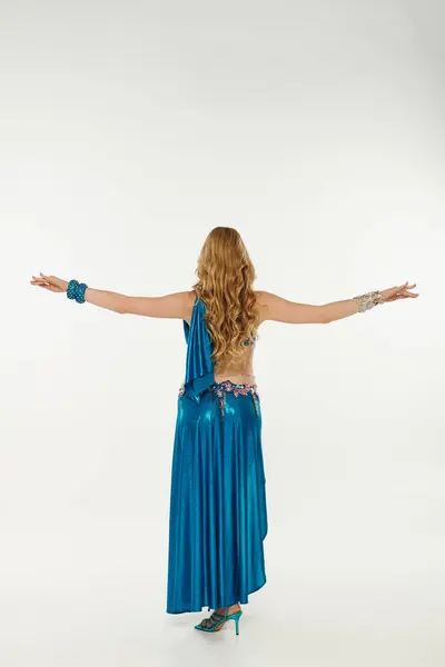 Young woman in a blue dress with arms outstretched while performing a belly dance. — Stock Photo