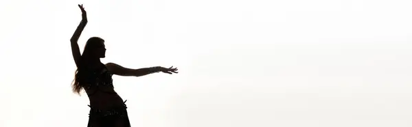 A woman in a flowing dress stands, arms raised in a joyful dance. — Stock Photo