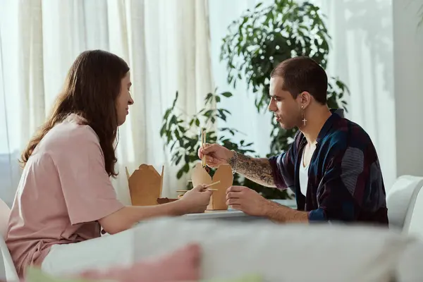 Una pareja gay con ropa casual se sientan juntos en una mesa, disfrutando de la comida y la compañía de los demás. - foto de stock