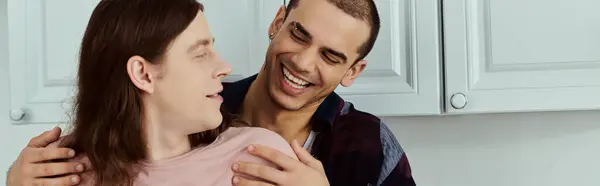 Um homem segura um parceiro ternamente em seus braços em uma cozinha aconchegante, ambos sorrindo e compartilhando um momento amoroso. — Fotografia de Stock