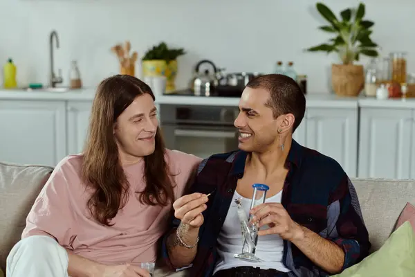 Homosexuelle Paare in lässiger Kleidung teilen einen gemütlichen Moment auf einer Couch, zünden Marihuana in der Glasbong an — Stockfoto